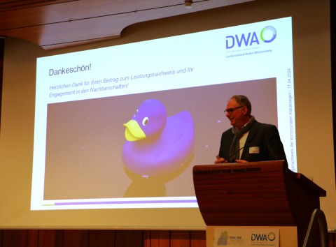 Alexander Weidelener steht rechts am Redepult. Hinter ihm ist auf der Leinwand eine Folie mit der DWA-Ente und Dankesworten f&uuml;r das ehrenamtliche Engagement der Lehrerschaft und Obleute zu sehen.