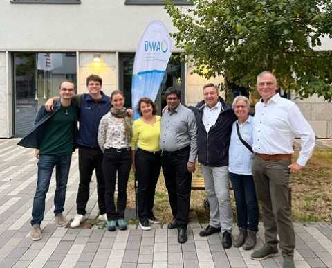 Mitarbeitende der DWA-Landesverb&auml;nde Baden-W&uuml;rttemberg und Hessen-Rheinland-Pfalz-Saarland stehen vor einem Geb&auml;ude sowie vor einer DWA-Fahne und einem Baum.