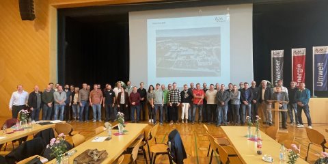Die Teilnehmenden des Treffens der Bodensee-Nachbarschaft stehen auf der B&uuml;hne des Sitzungssaals. Im Vordergrund Tische und St&uuml;hle, im Hintergrund eine Leinwand.
